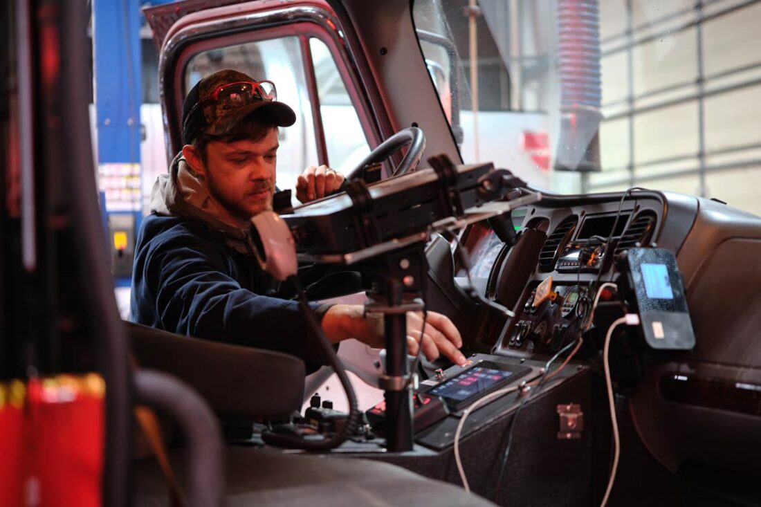 Central Garage at work - Gallery image A mechanic working on the dashboard controls of a truck cab, with diagnostic equipment mounted near the steering wheel