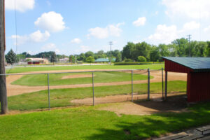 A photo looking out over the fence of Rogers Park's baseball diamond on a sunny day.